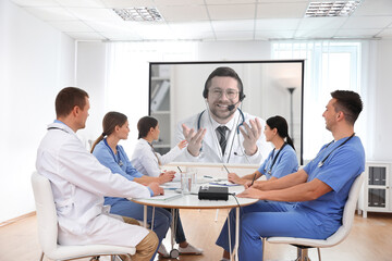 Team of doctors using video projector during conference indoors. Speaker on projection screen