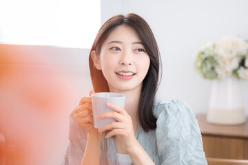 部屋で飲み物を飲んでリラックスするかわいい若い女性　のんびりティータイム