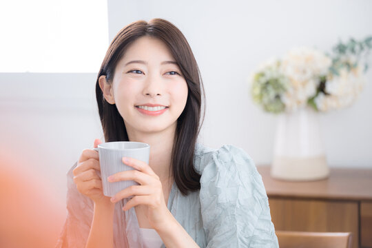 Cute young woman relaxing with a drink in her room. Leisurely tea time.