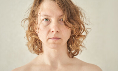 Caucasian adult female with curly hair staring directly at camera against neutral background.