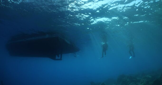 Scubadivers around the dive boat underwater with sun beams and rays