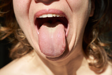 Close-up of caucasian female with open mouth and extended tongue in bright light.