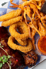 A colorful assortment of food includes crispy onion rings, tender barbecue ribs, and sweet potato fries presented on a festive platter at a lively outdoor festival, enticing visitors