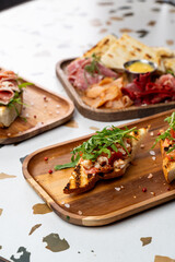 Freshly grilled crostinis topped with colorful ingredients sit on rustic wooden platters, surrounded by an array of charcuterie delights at a lively eatery