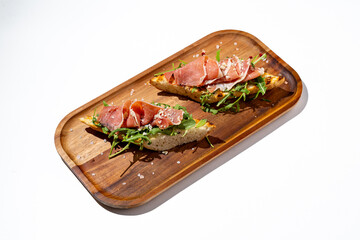 Artisanal toast featuring fresh arugula and thin slices of cured meats rests on a rustic wooden platter, evoking a taste of gourmet simplicity and culinary creativity