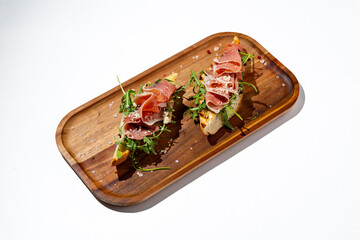 Two stunning open-faced sandwiches rest on a warm wooden serving board
