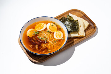 Ramen filled with rich broth showcases soft-boiled eggs, succulent meat, and seaweed. A wooden platter complements the dish with a side of fresh bread, perfect for any mealtime