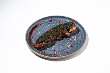 A beautifully presented steak lies on an elegant plate, adorned with a rich herb crust and vibrant pink peppercorns. The dish showcases culinary artistry and attention to detail