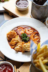 Savory shrimp surrounded by rich sauce and fluffy bread rolls on a bright plate creates an appetizing display in a lively eatery at midday, enticing diners with flavor