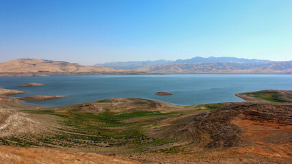 Vast landscape of a serene lake surrounded by hills and mountains during a clear sunny day