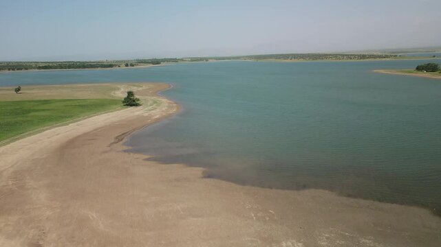Aerial view of green peninsula and grazing herd by Djizak Reservoir