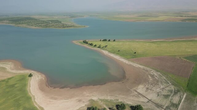 Aerial: winding sandy coves and emerald water meeting Uzbek farmlands in light