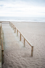 Naklejka premium Access to the beach is through a wooden bridge on a gray, sunless day.