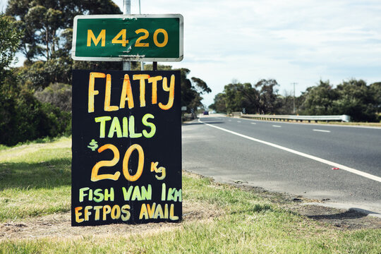 Close up of orange and yellow roadside sign advertising flathead tails