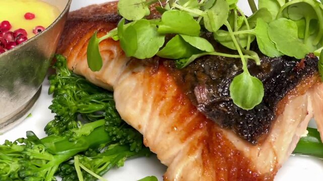 Salmon fillet with crisp skin, served with tenderstem broccoli, microgreens and creamy peppercorn sauce in London, slow motion