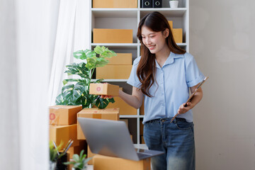 Asian woman entrepreneur taking notes while working on laptop a customer managing orders in her sme...
