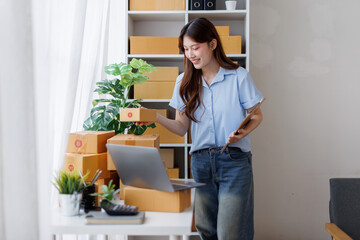 Asian woman entrepreneur taking notes while working on laptop a customer managing orders in her sme...