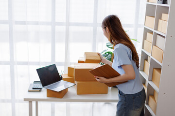 Asian woman entrepreneur taking notes while working on laptop a customer managing orders in her sme...