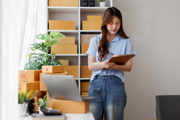 Asian woman entrepreneur taking notes while working on laptop a customer managing orders in her sme...