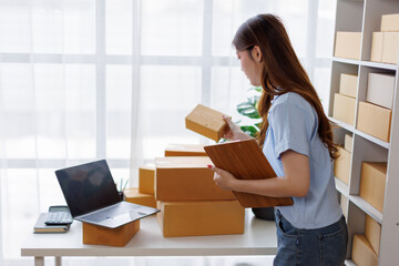 Asian woman entrepreneur taking notes while working on laptop a customer managing orders in her sme...