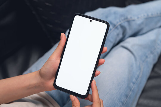 Hand holding smartphone with blank screen for graphic display montage on the sofa in the living room, mockup display for lifestyle and wireless technology.