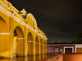 Historic yellow archways illuminated at night in Antigua Guatemala with dark sky and reflections