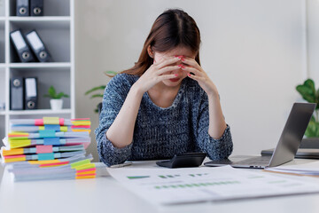 Young asian woman accountant employee Upset stressed guy suffering job problems working on laptop, headache, Bored workaholic headache and stress, migraine, stress relief, chronic pain
