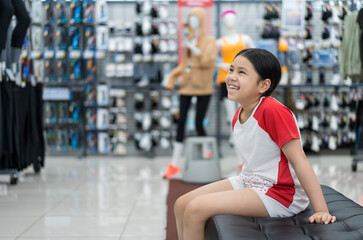 sport girl by asian child or young kid sitting relax happy smile on black sofa chair to shopping sports equipment in department store or mall on summer holiday for exercise and healthy with copy space