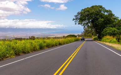 A car drives on a road with a view of the ocean and sky.