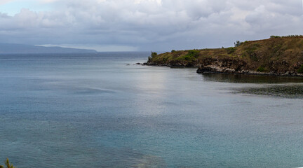 Overcast day at the coast with a rocky cliff and calm water.