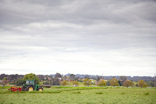 Green tractor pulling red slasher in lucerne paddock