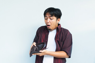 Asian Indonesian man showing his empty wallet with sad and worried expression. Isolated in gray...