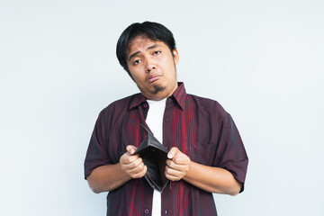 Asian Indonesian man showing his empty wallet with sad and worried expression. Isolated in gray background.