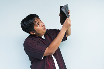 Asian Indonesian man showing his empty wallet with sad and worried expression. Isolated in gray background.