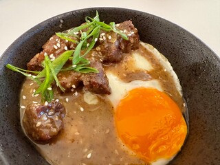 A bowl of rice with roasted beef, fried egg, sesame seed, and special sauce