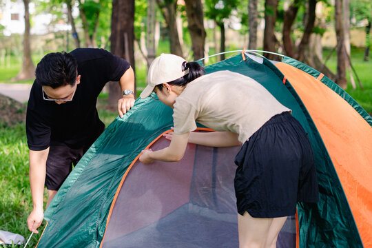 Couple setting up a camping tent in a spacious park during a sunny day surrounded by trees