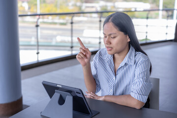 Young Asian woman working on tablet with stylus, focused and productive in a modern indoor/outdoor...