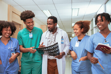 Group of medical students walking in a hallway at medical university. Focus is on African American male student.African doctors discussing MRI scan film on a hospital corridor in background.