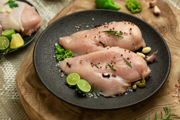 Raw chicken breast with lemon and spices, ready to cook, wooden background.