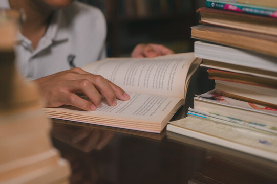 Hand of young man reading a book in library room with blurred book shelves background in concept of knowledge is power research and education development