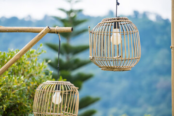 Two bamboo lanterns hanging outdoors with a lush green mountainous backdrop creating a serene and natural ambiance