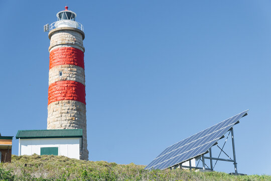 A stone lighthouse on a hill next to an array of solar panels