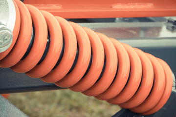 Red hard spring made of steel. Part of big industrial or agricultural machine