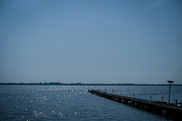 A long jetty extends into a calm, sun-drenched lake under a clear sky. The Dümmer, also referred...