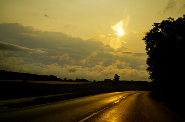 A paved road leads into a sunrise with dramatic clouds and a tranquil atmosphere. Morning path, sun...