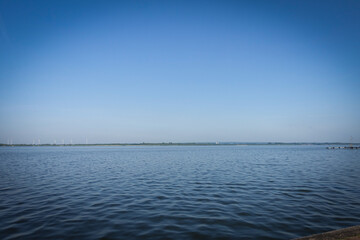 A sweeping view of a tranquil lake stretching beneath a pristine blue sky. The Dümmer, also...
