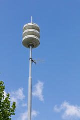 A modern civil defense siren and antenna stand against a clear blue sky with sparse clouds, ready to alert the community.