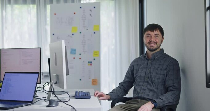Portrait confident smiling male programmer working with robotics code AI software and looking at camera in tech office. Artificial intelligence dashboard, robotics, user interface, machine learning.