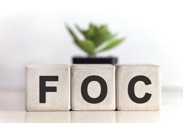 FOC - Free of charge concept on wooden cubes and flower in a pot in the background