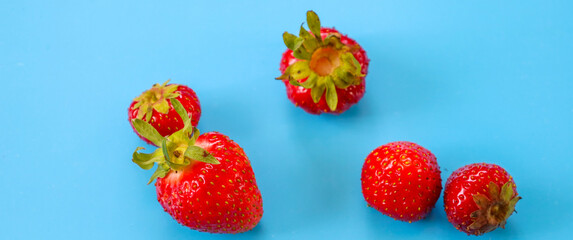 Bright red strawberries are scattered haphazardly on a vibrant blue background, creating a dynamic and appealing composition. This striking contrast is ideal for summer and culinary themes.